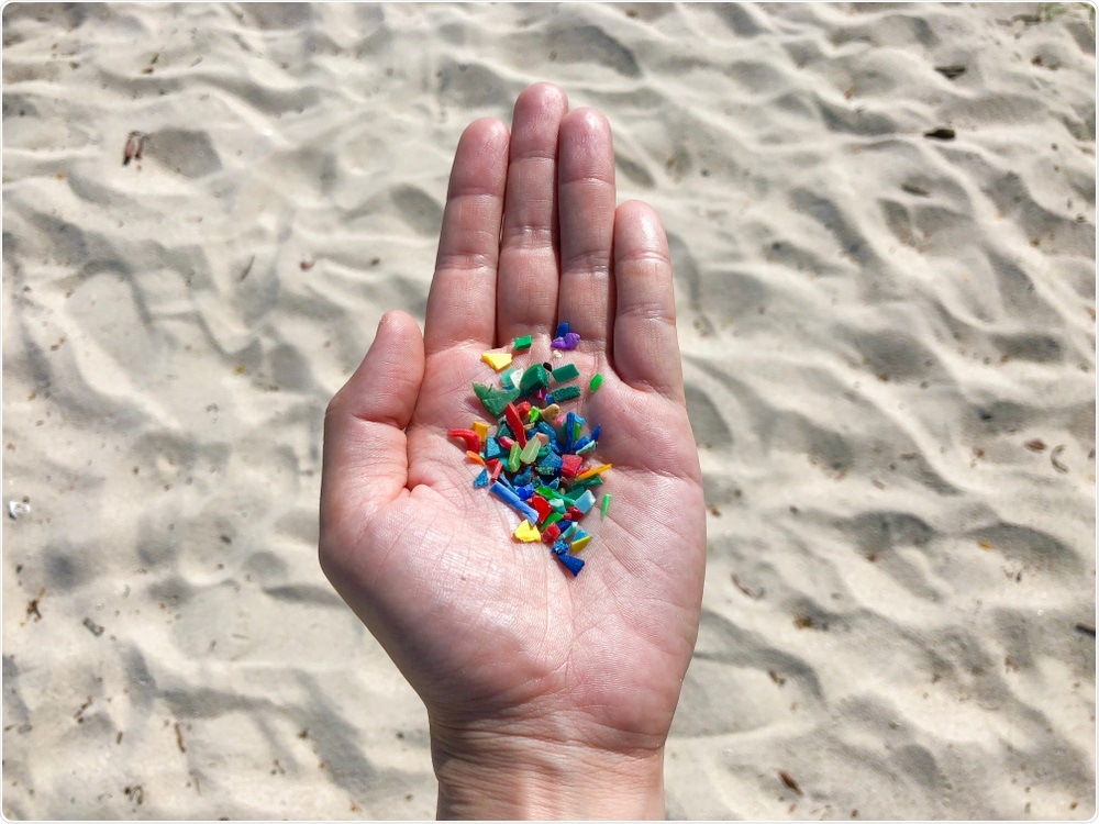Microplastic in palm of mans hand, sand in background - By Loretta Sze