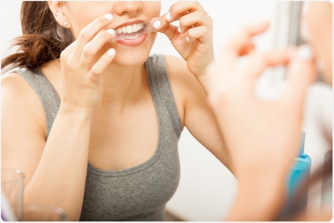 Woman applying a whitening strip on her teeth. Image Credit: antoniodiaz / Shutterstock