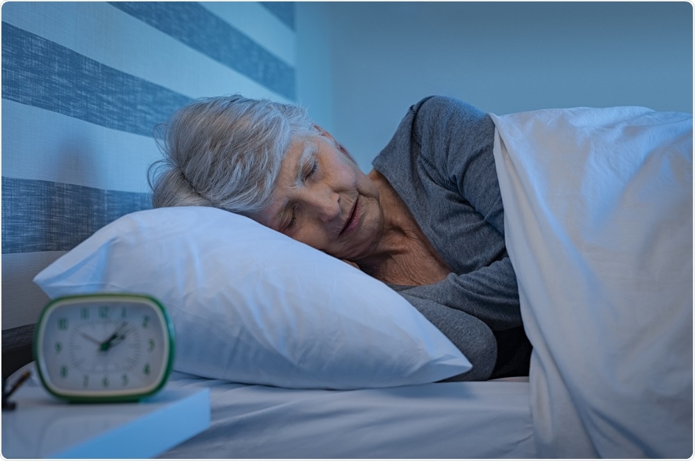Older adult sleeping in bed, with alarm clock in forefront