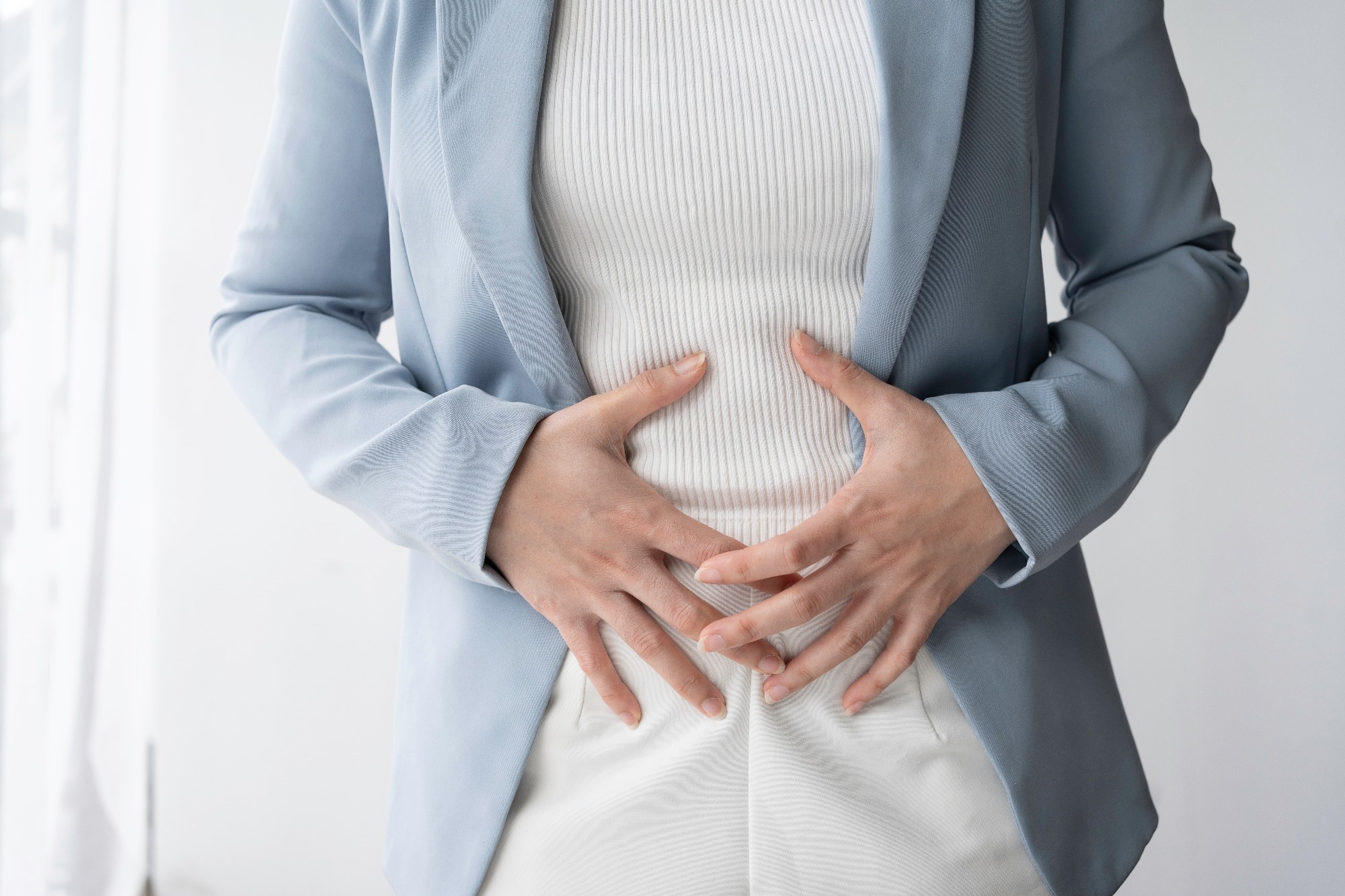 Businesswoman is standing in her office, holding her stomach in pain, possibly experiencing digestive problems