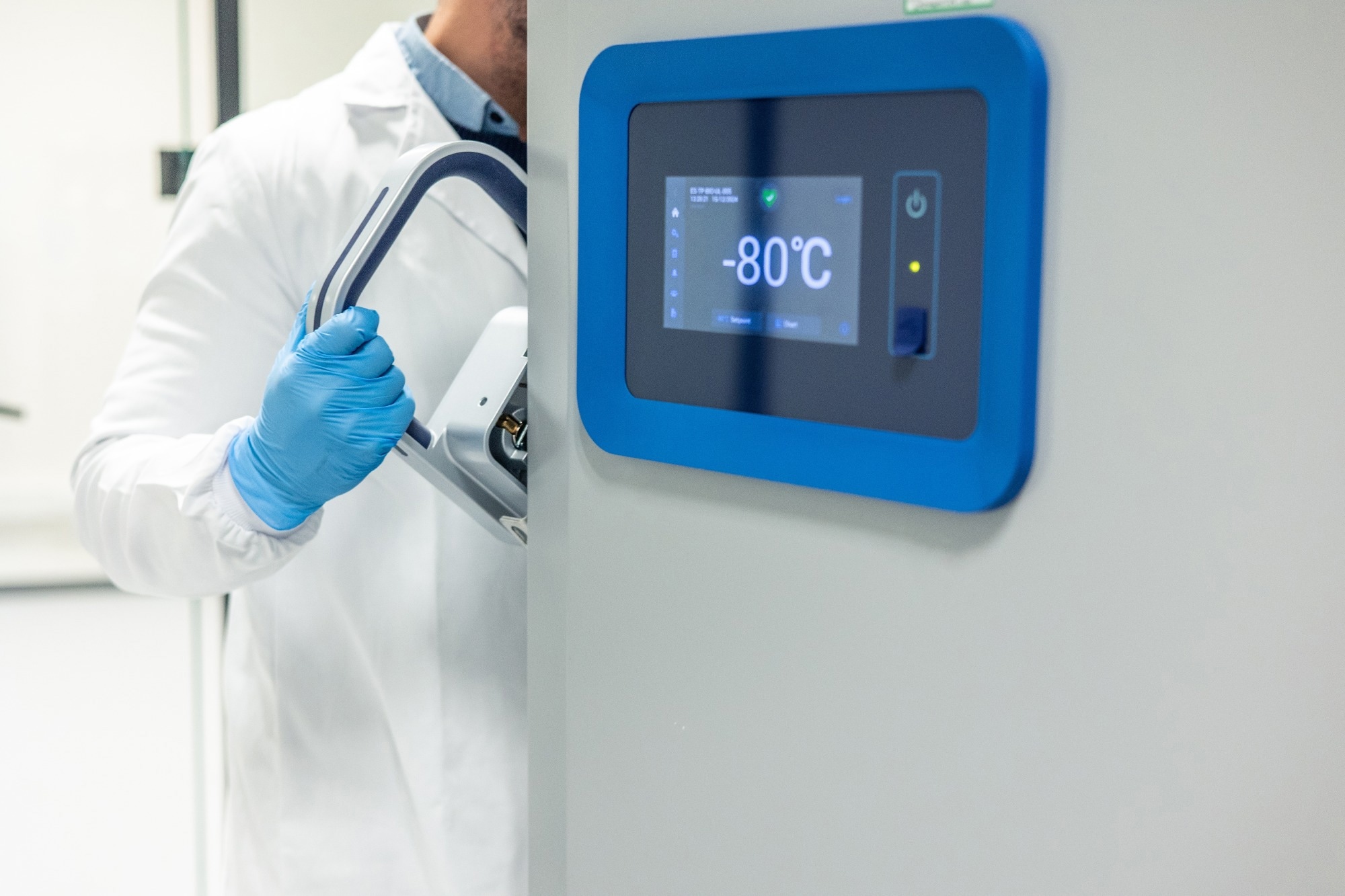 Scientist wearing sterile blue gloves and white lab coat opening cryogenic freezer storing samples at -80 degrees Celsius in scientific laboratory