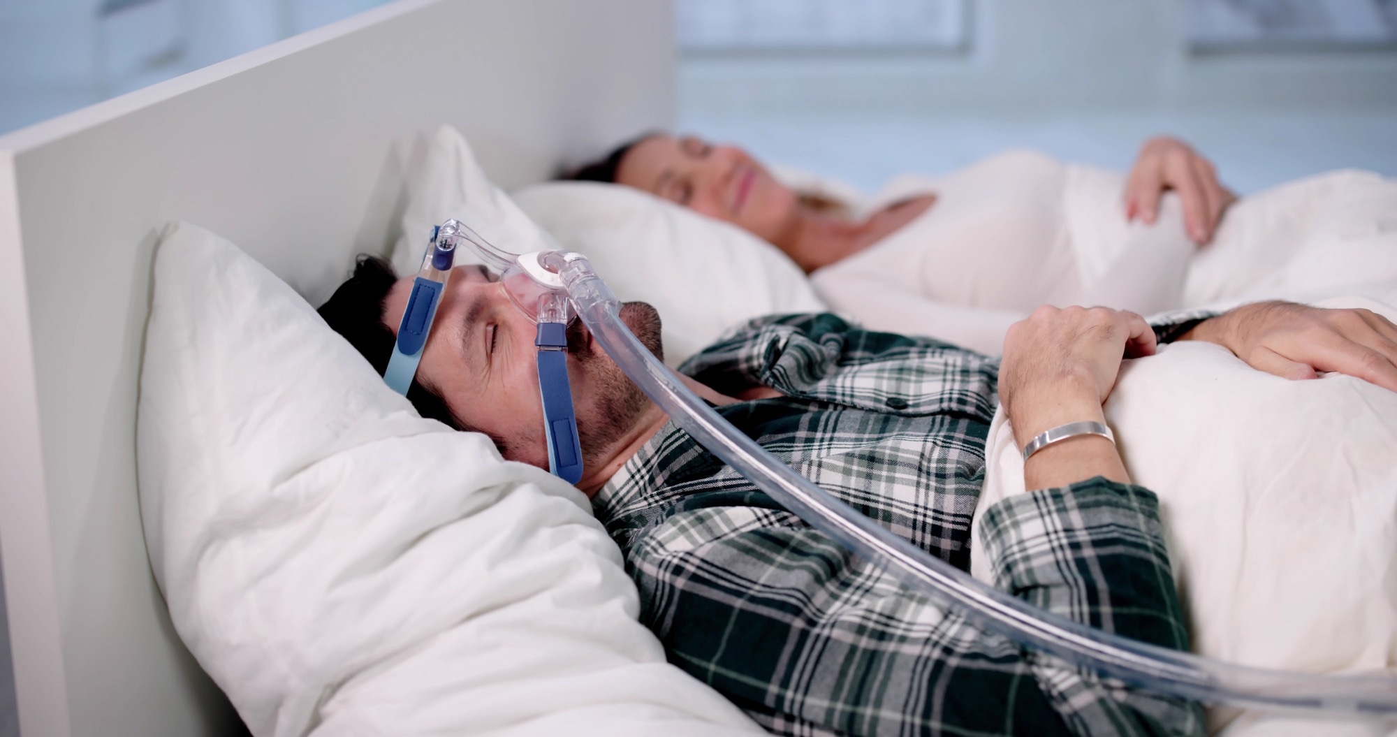 Man sleeping in bed with wife, wearing sleep apnea mask