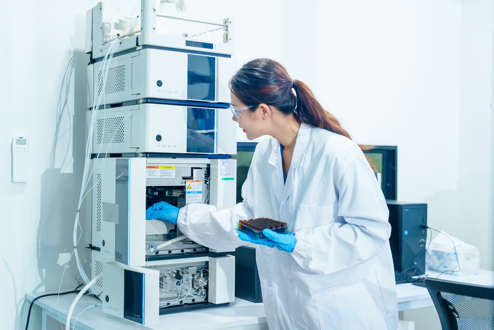 Researcher handling a multiwell sample plate beside analytical laboratory equipment.