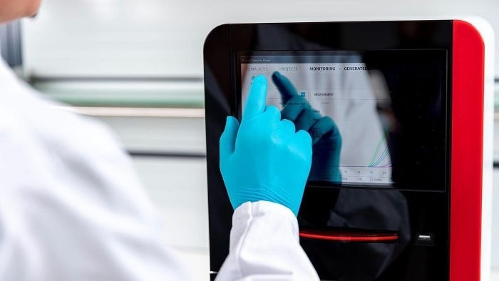A person wearing a lab coat and blue nitrile gloves keys in parameters on the qTOWERiris touchpad.