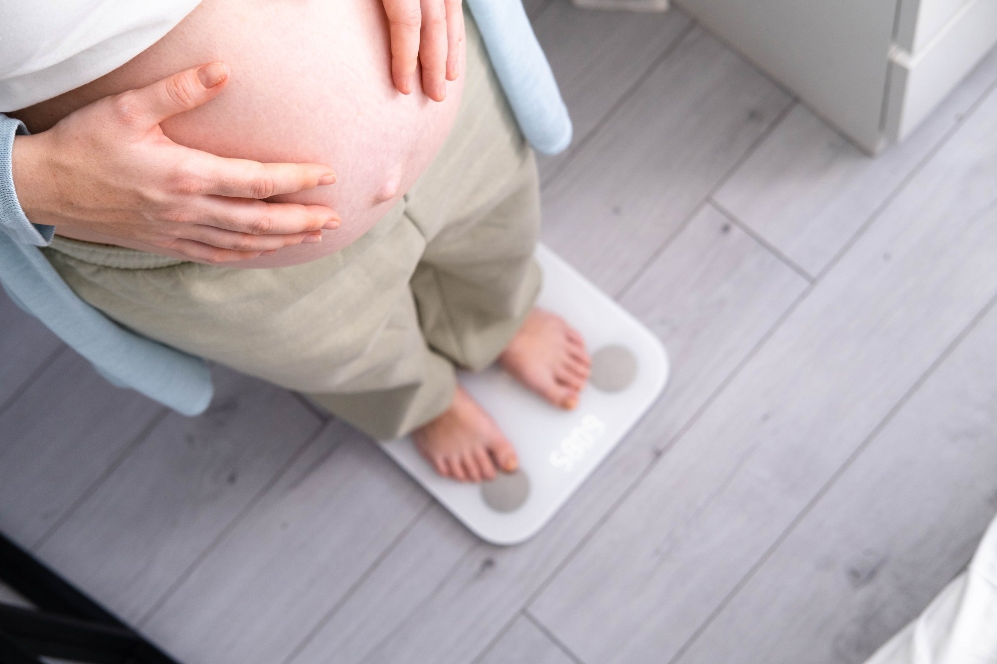 Young woman measuring her pregnant weight standing on scales.