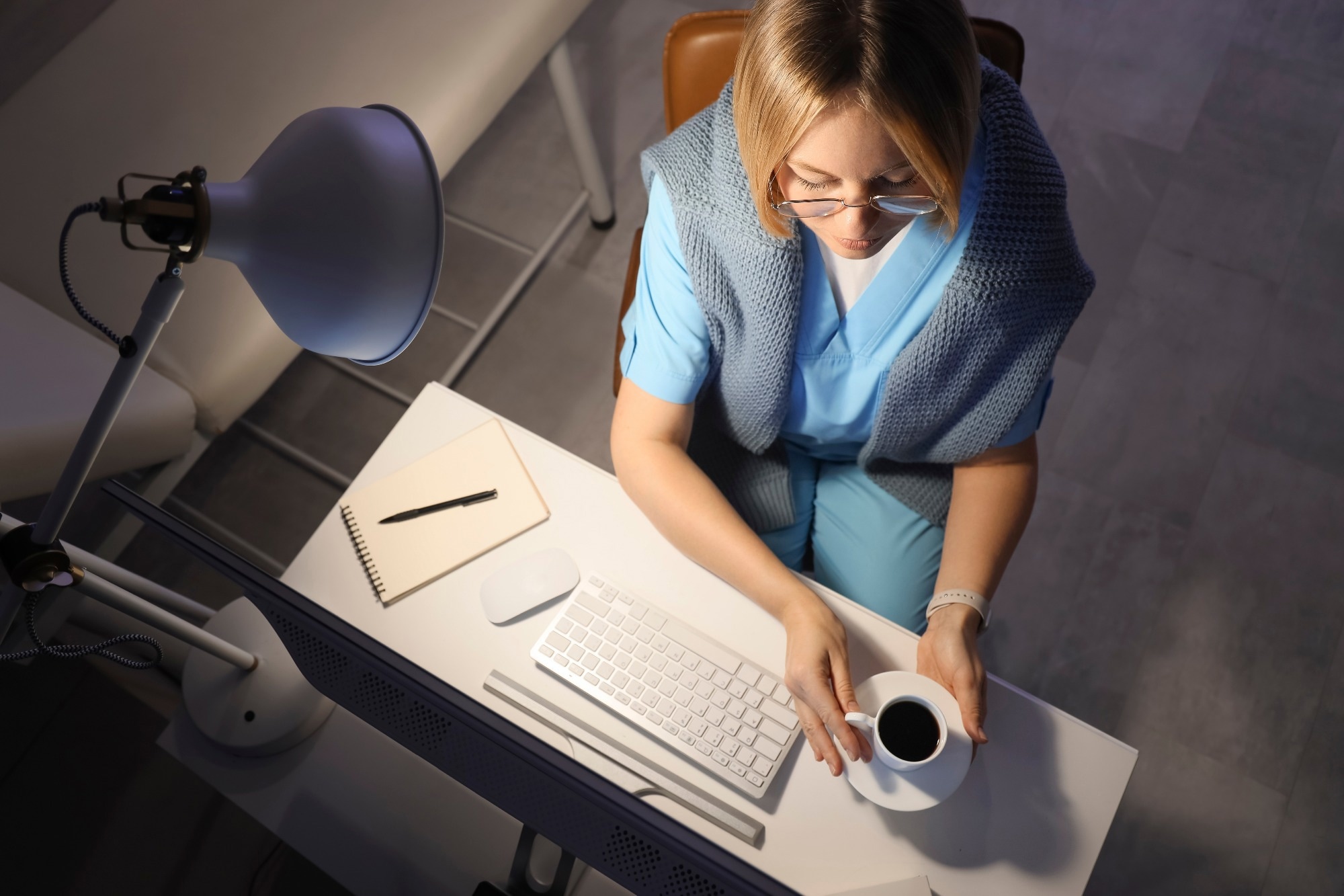 Female nurse with cup of coffee working evening shift at table in clinic