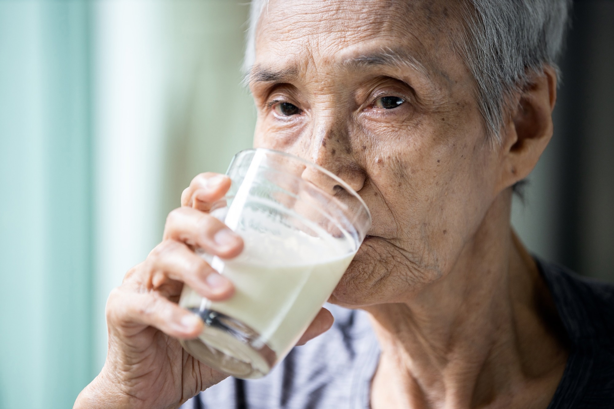 Asian senior woman drinking warm fresh milk from glass in the morning at home