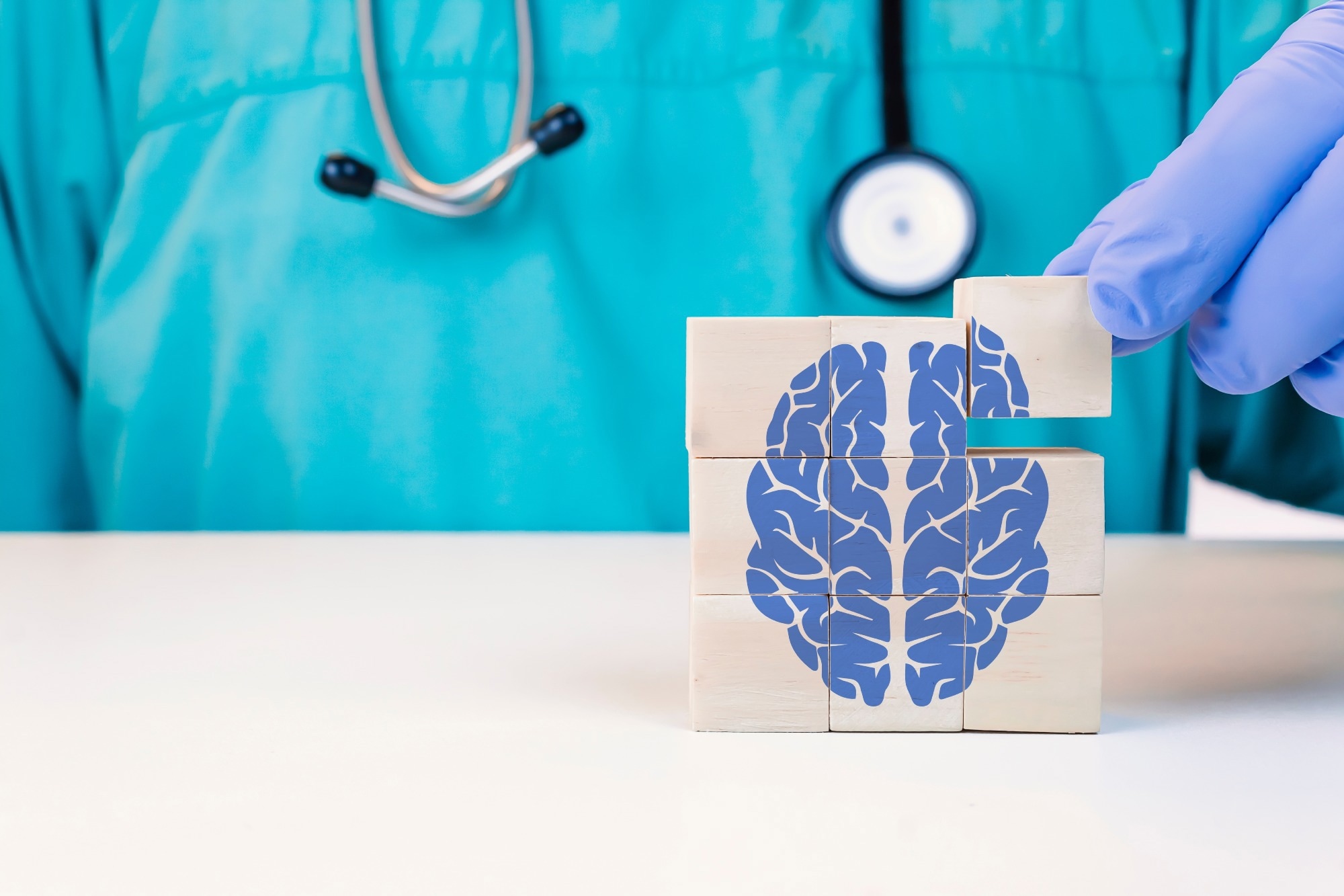 Doctor gloved hand stacking wooden blocks to form a square cube with a blue brain image on them