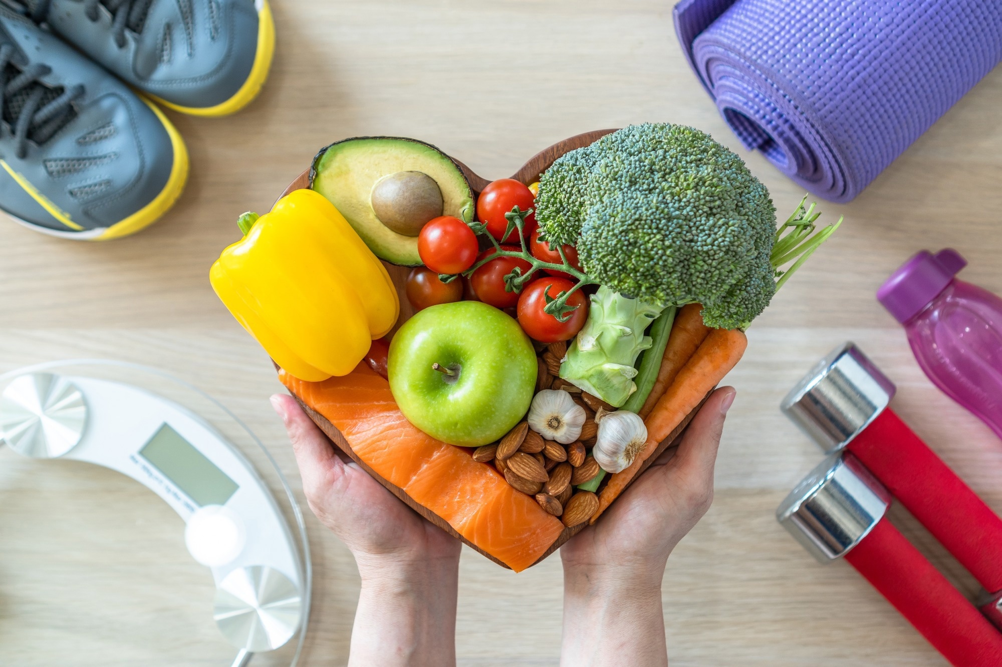Heart shaped plate filled with vegetables. Background shows running trainers, small dumbbells and scales for heart health and nutrition concept