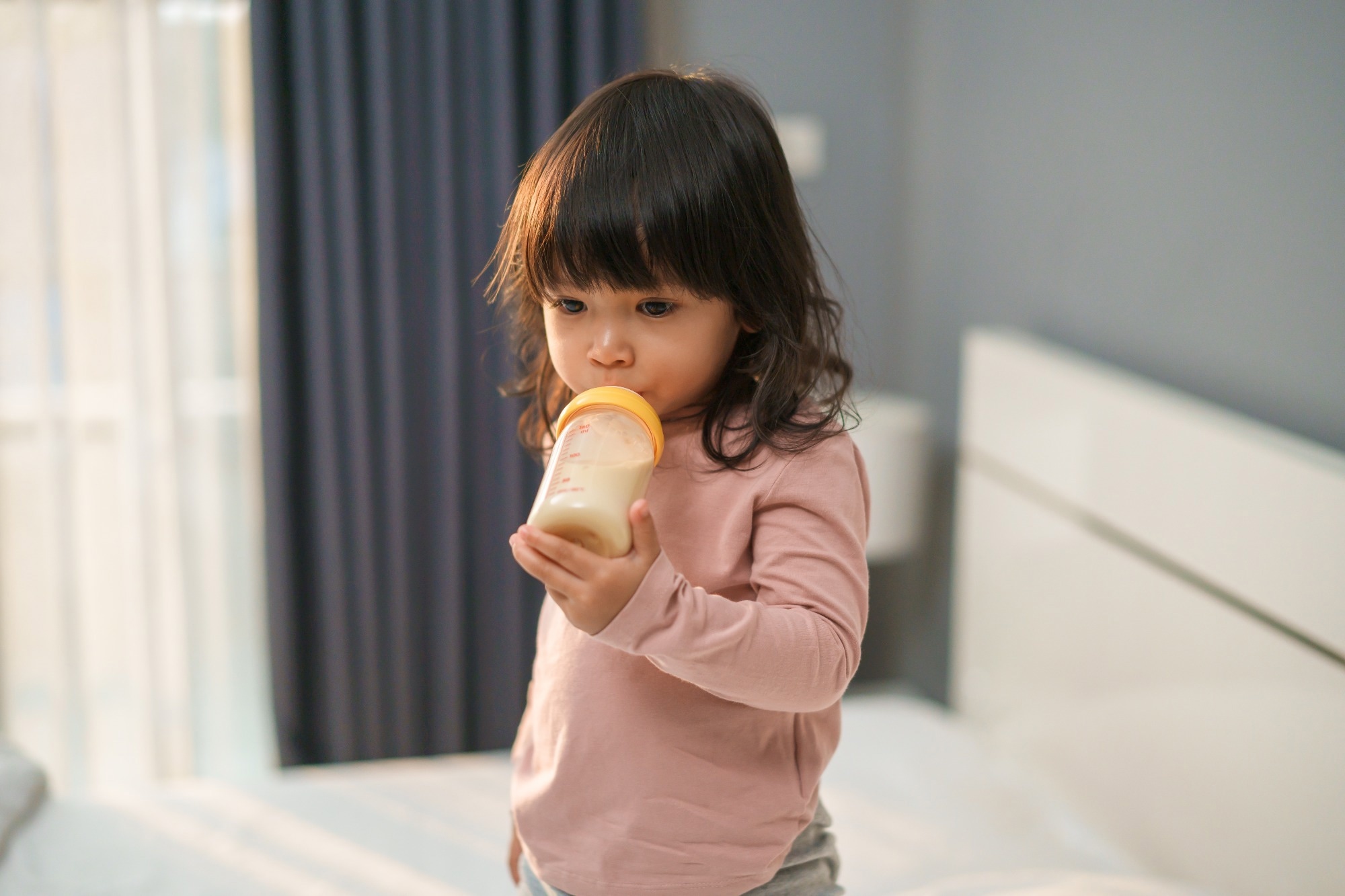 toddler girl drinking milk from bottle on a bed