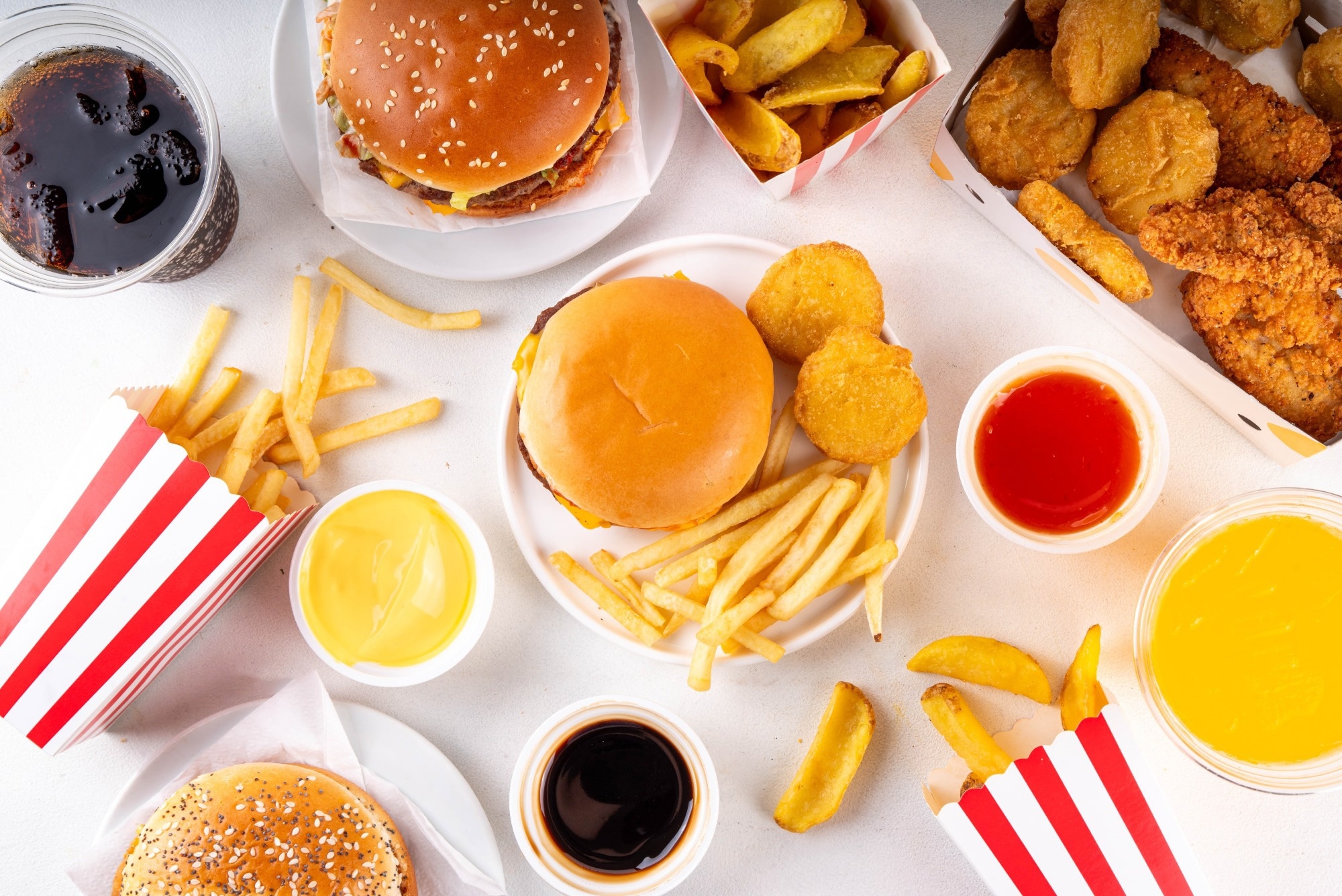 Fast food delivery menu background with various burgers, cheeseburger, nuggets, french fries, fizzy soda drinks. Junk unhealthy fast food, Ultra processed food with low nutrition, high calories value