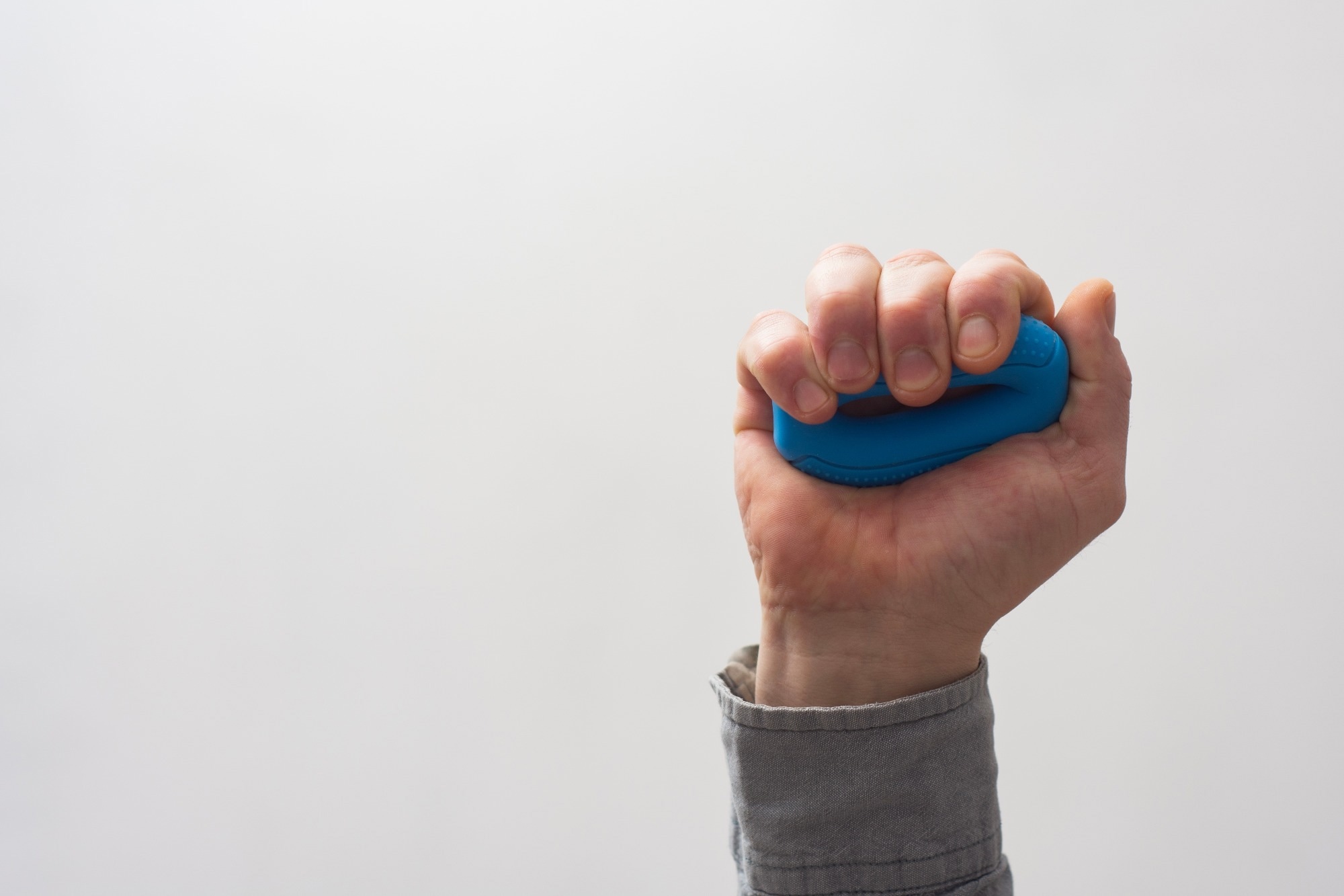 Hand firmly grips a blue resistance trainer against a white background. Concept for fitness enthusiasts and physical therapy exercises