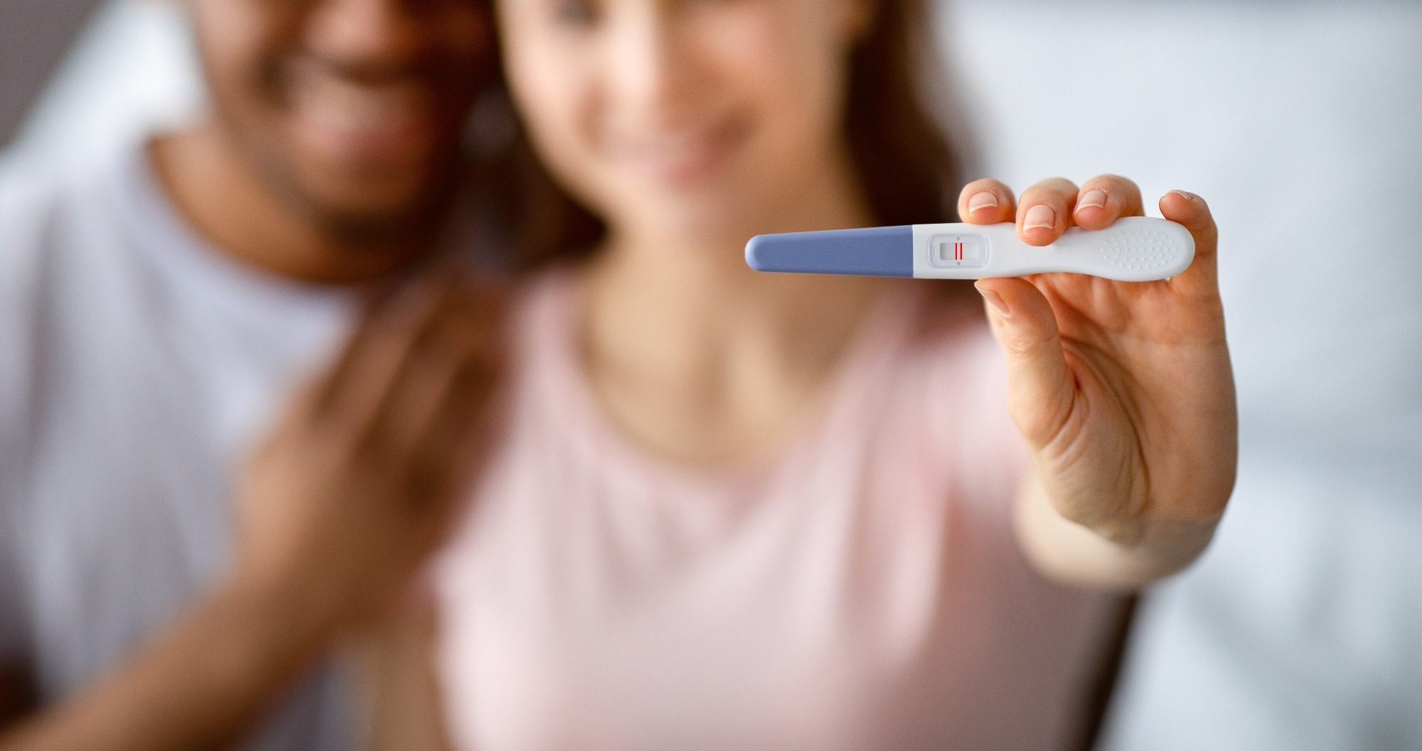 Happy multiracial couple in love showing positive pregnancy test on camera, selective focus
