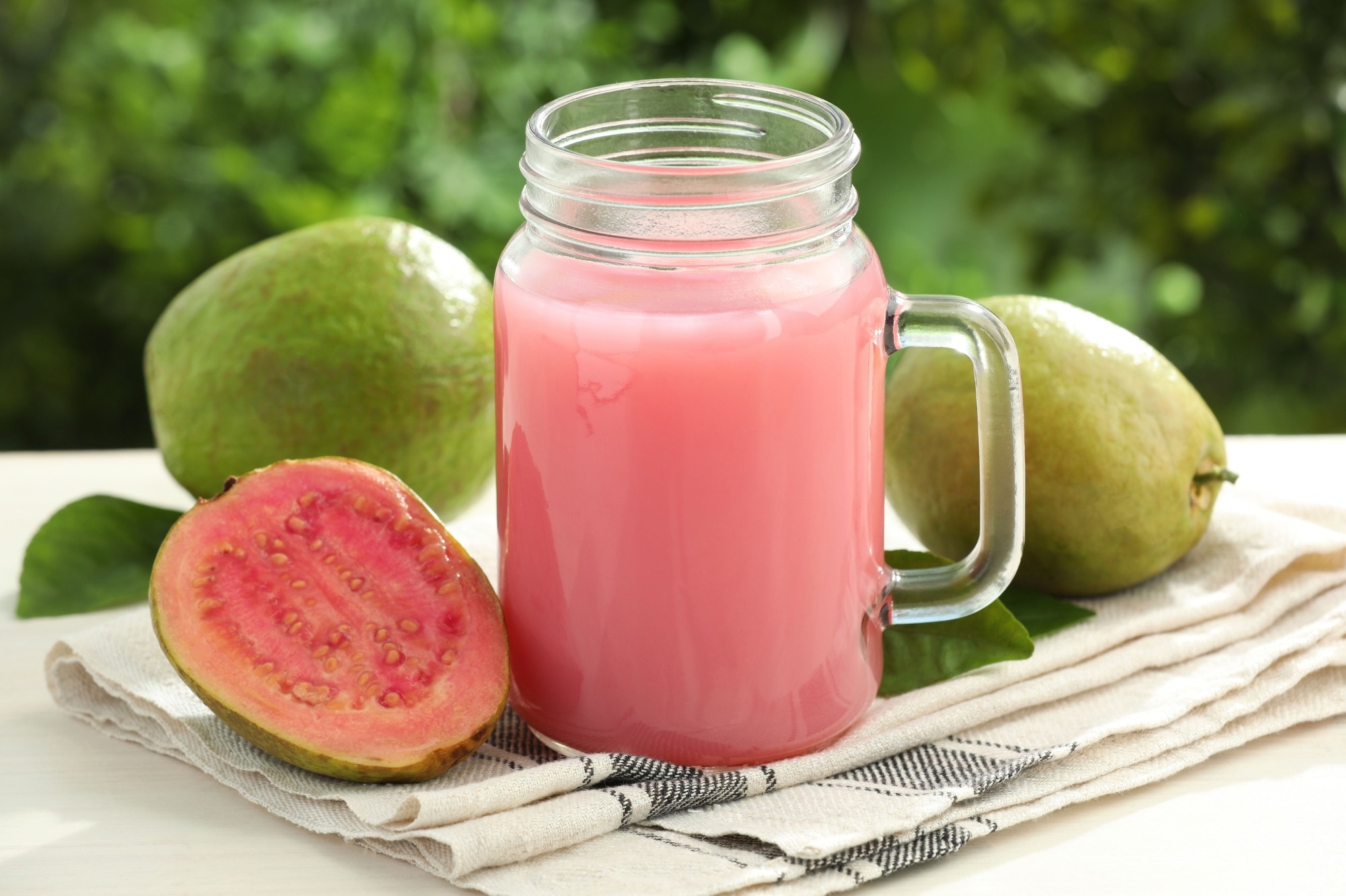 Delicious guava juice in mason jar and fresh fruits on outdoor white table, closeup