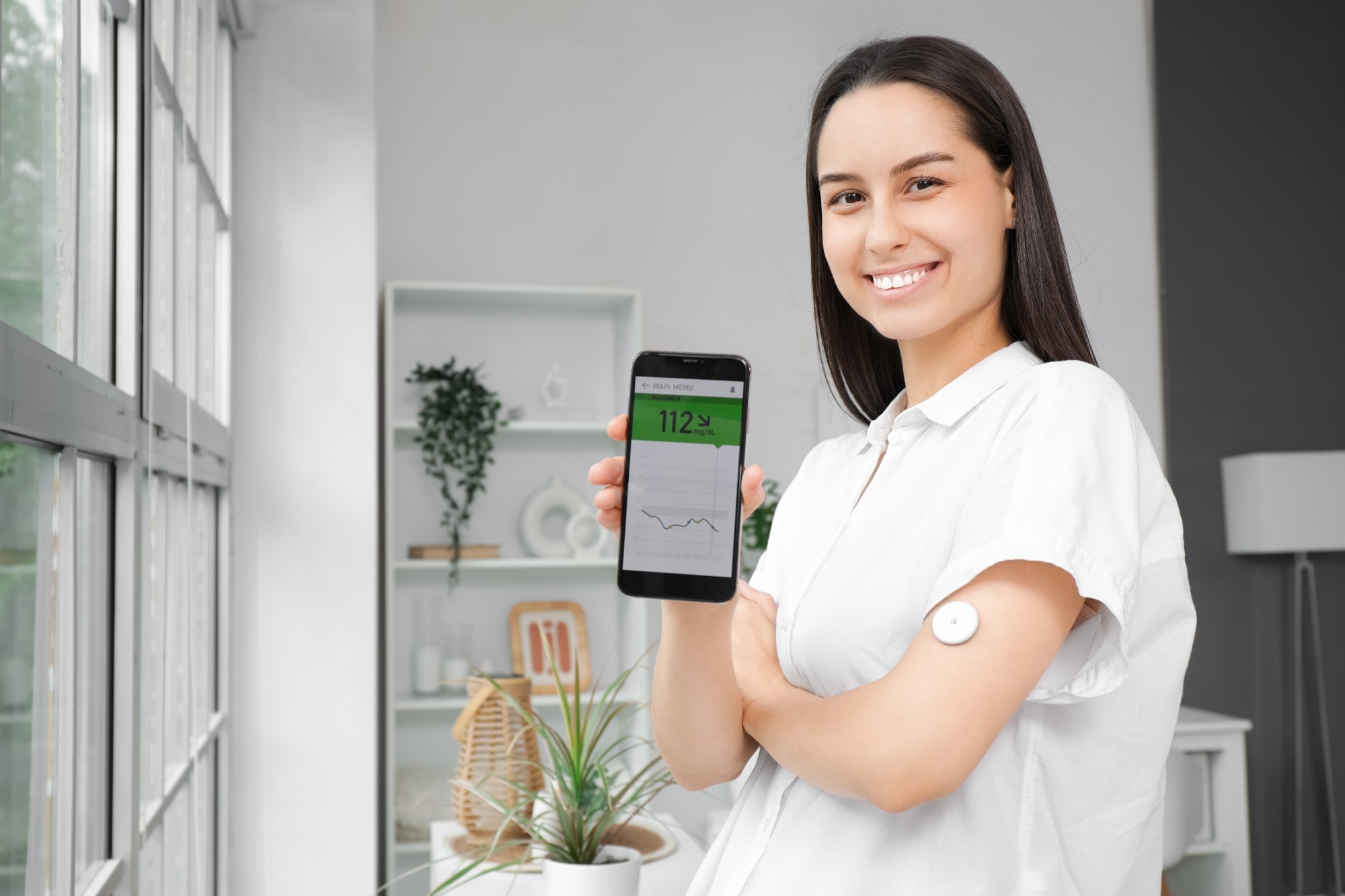 Diabetic young woman with glucose sensor and mobile phone at home