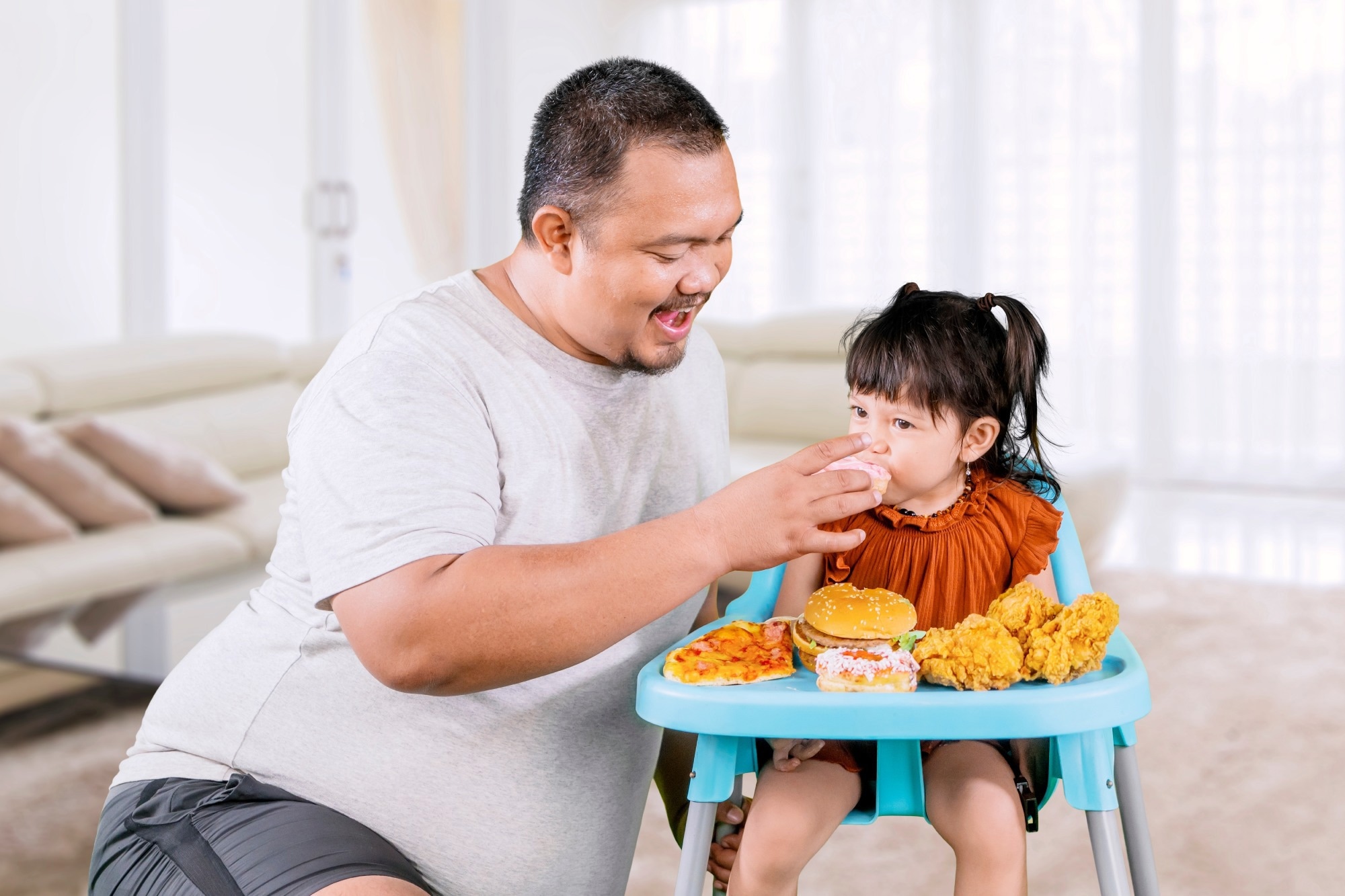 Overweight father gives daughter unhealthy junk food on high chair at home