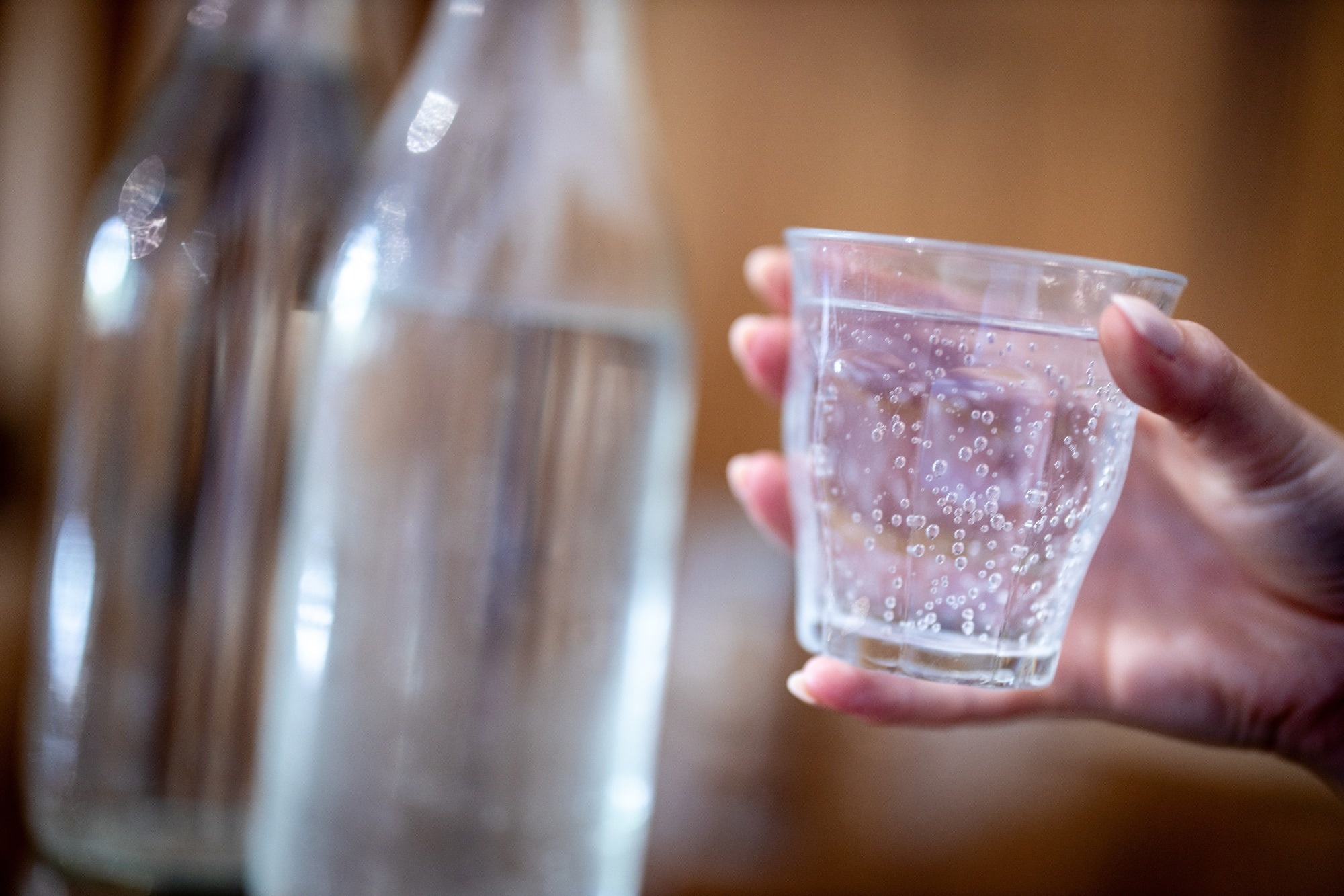 Hand holding a small glass of fizzy, sparkling water
