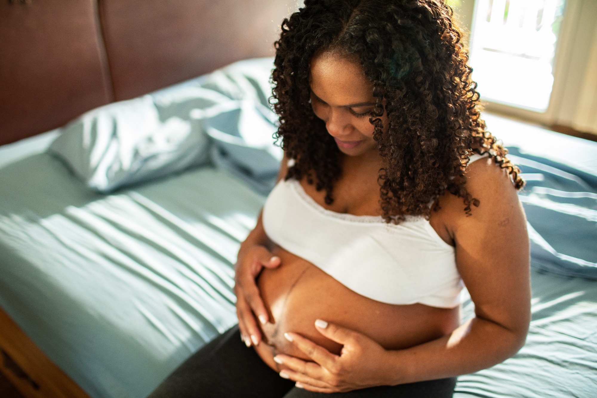 Pregnant woman holding belly in bed at home
