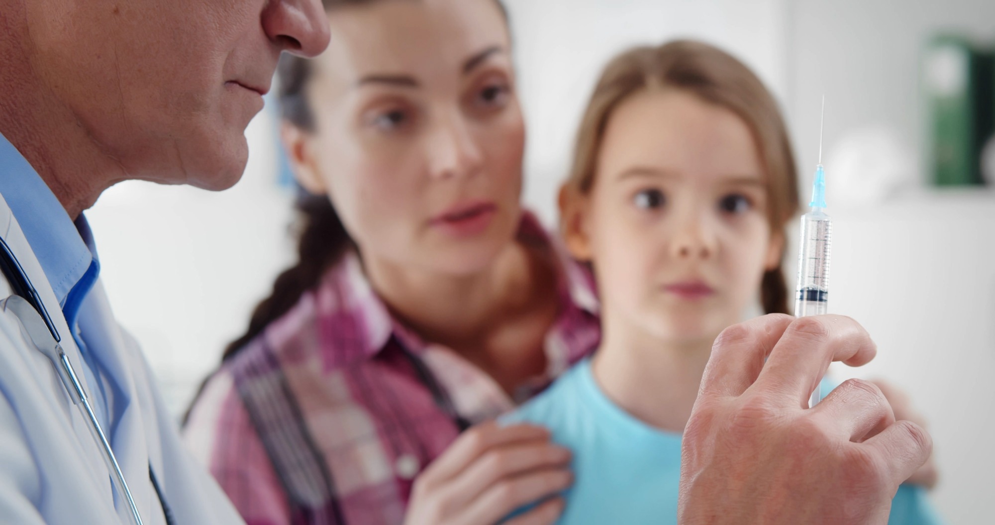Little girl worried during vaccination in clinic office. Close up of mature pediatrician holding syringe with medication vaccinating cute child in hospital office