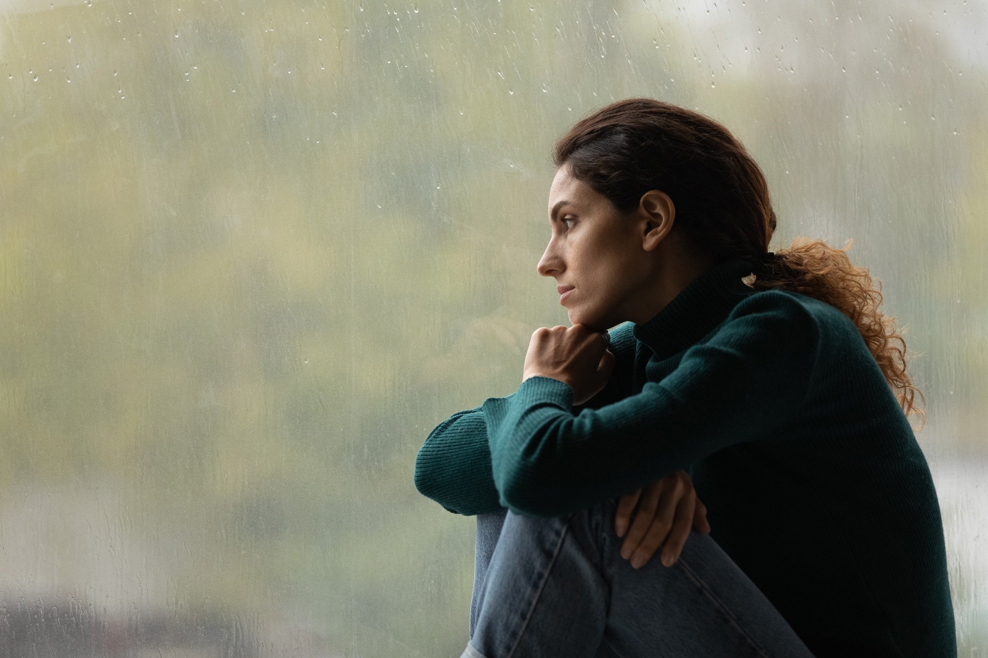 Side view frustrated thoughtful woman looking out rainy window in distance alone, lost in thoughts
