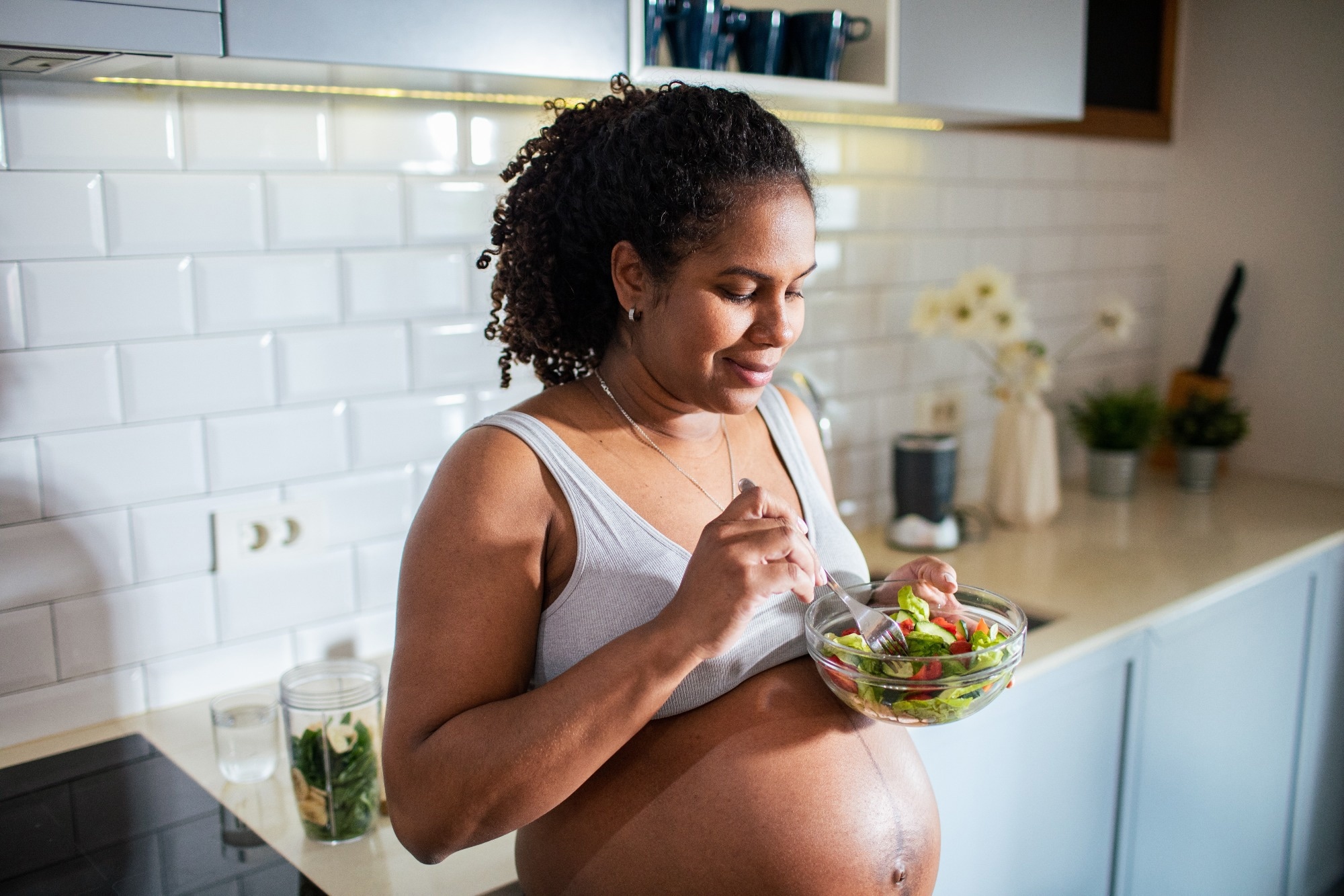 Young Latina pregnant woman eating salad in the kitchen at home