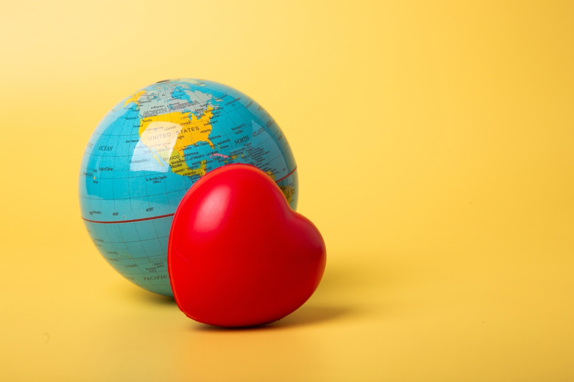 Red heart resting against a world globe on a yellow background