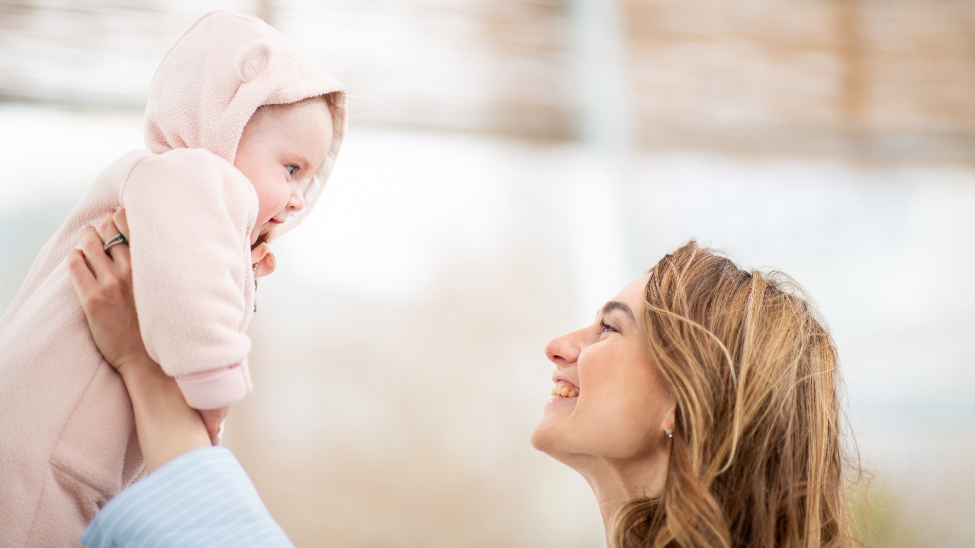 joyful mother lifts her smiling baby into the air while keeping tender eye contact