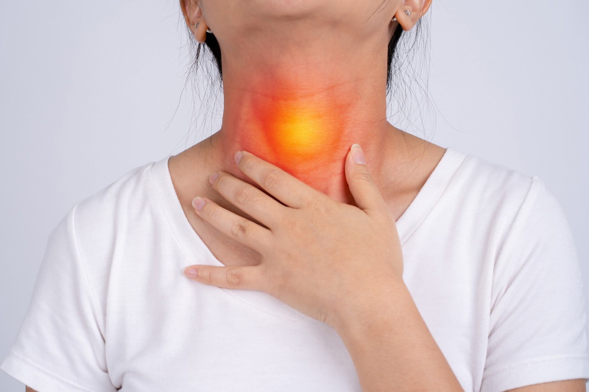 A woman holds her hand to the front of her neck, with a red and yellow glow highlighting the throat area to represent pain or discomfort.