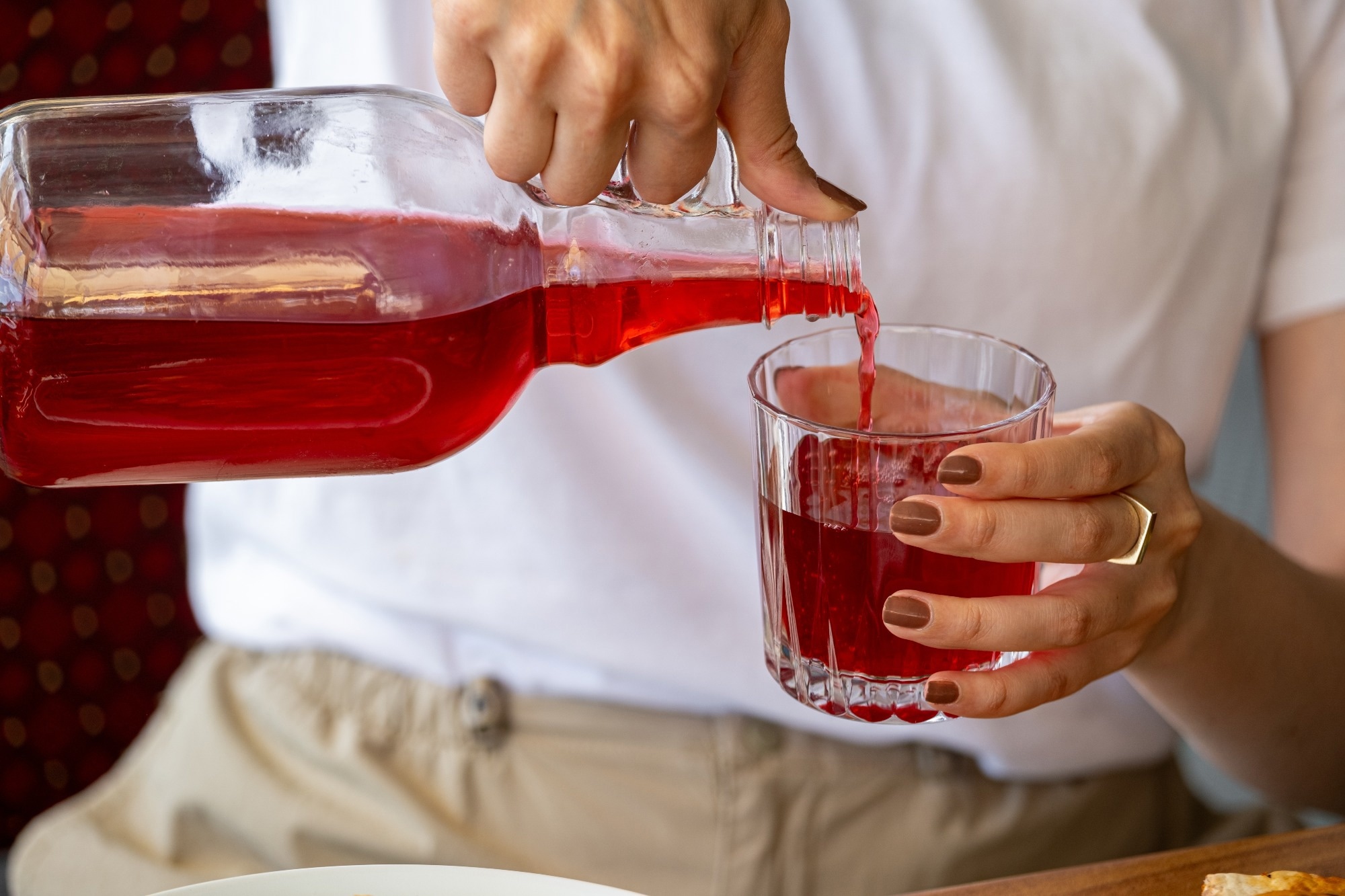 Hands of a woman pouring red cranberry juice from a jug into a glass