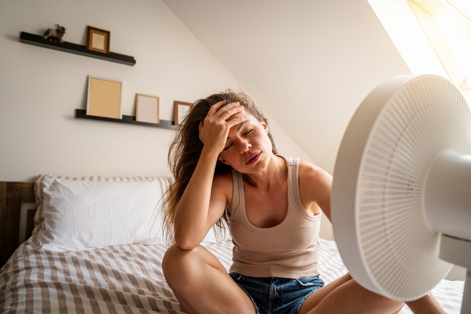 Overheated woman trying to cool down with fan at home
