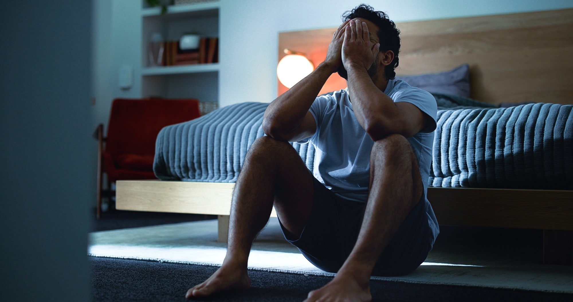 Man sitting on the floor at the edge of a bed. Head in hands